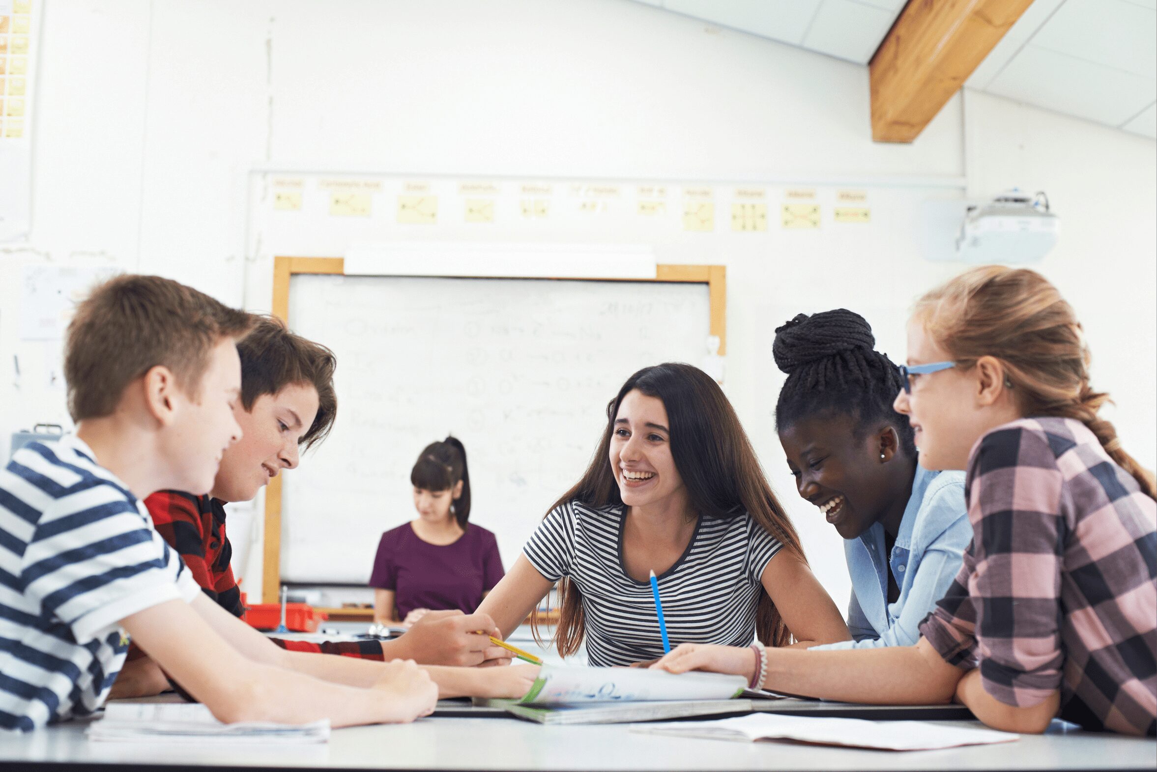 A group of teenage students smiling and laughing together while they work on a task in class.