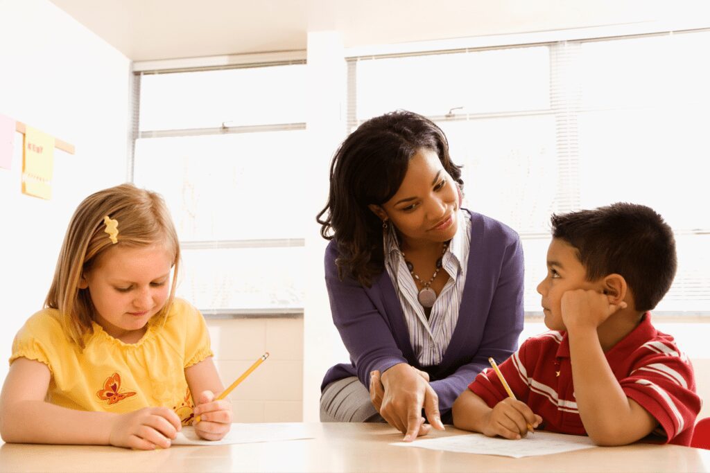 Female teacher helping two young students with their work.