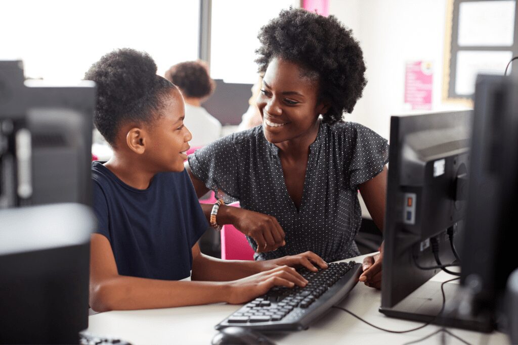 Young female teacher helping a middle school aged student on the computer. Both are smiling.