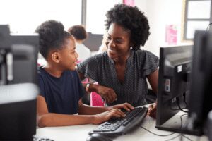 Young female teacher helping a middle school aged student on the computer. Both are smiling.