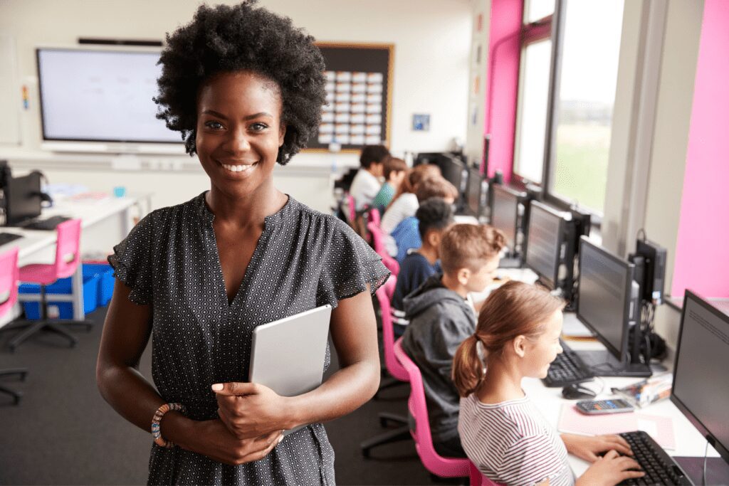 Substitute teacher smiling while her students work on computers in the background.