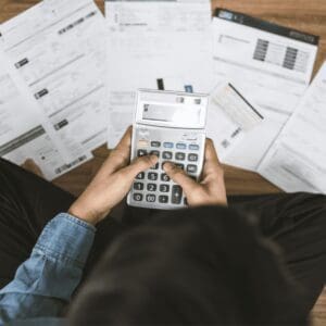 A young relief teacher is sitting on the floor surrounded by pieces of paper with a calculator trying to calculate their income tax.