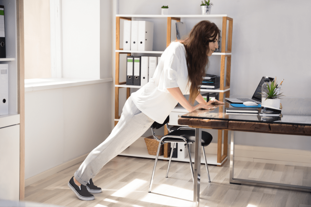 Teacher leaning on her desk to exercise while at work.