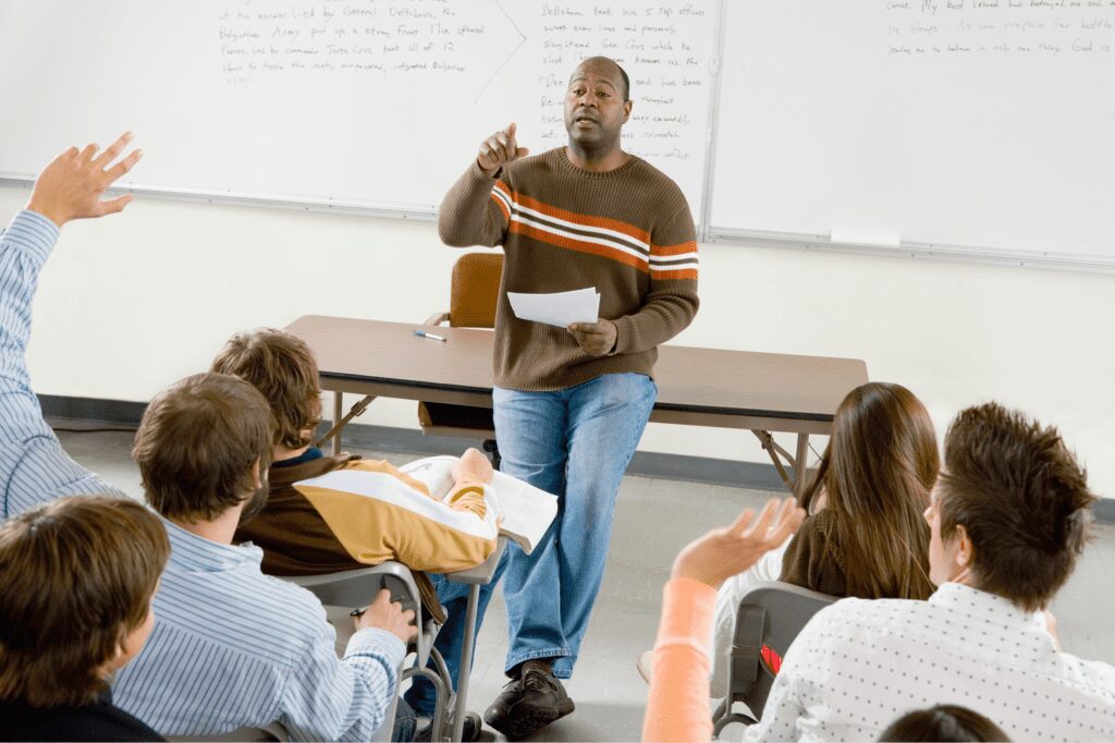 Teacher who is an expert in his subject lecturing a class of students from the front of the classroom.