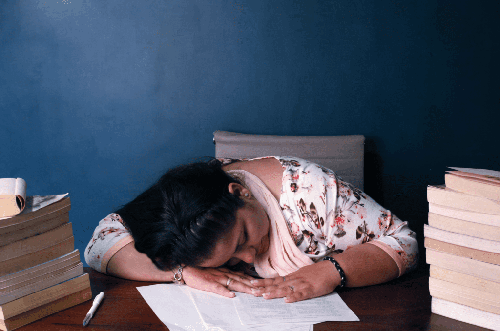 Teacher falling asleep at her desk because she has poor work-life balance.
