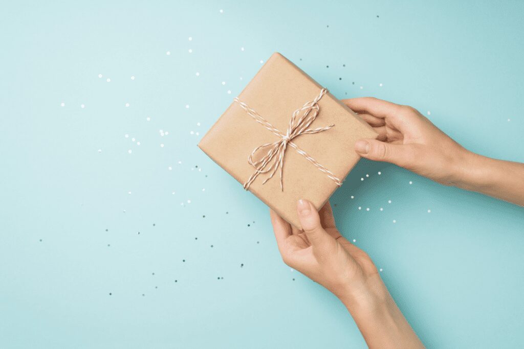 A blue background with a gift wrapped in brown paper with a string bow being held by two hands.
