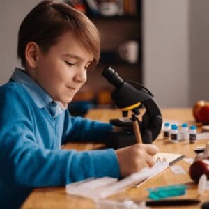 A homeschool student is sitting at his desk with a microscope and a pad of paper.