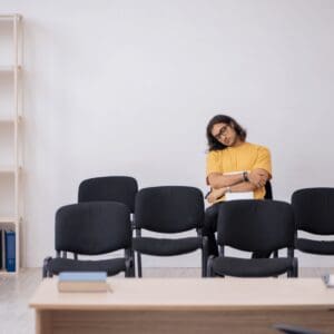 A woman is sitting in an empty room with chairs.
