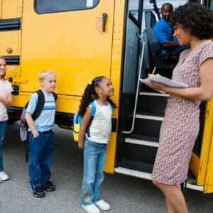 A teacher is marking attendance as her students get on the school bus.