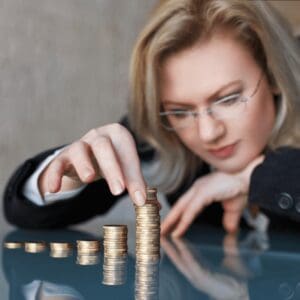 A woman is stacking coins on top of a classroom table.