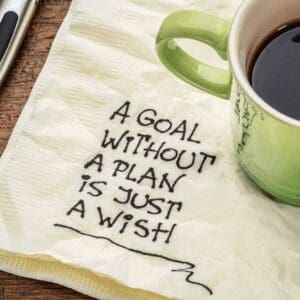 A coffee cup is sitting on a napkin. On the napkin is written "A goal without a plan is just a wish".
