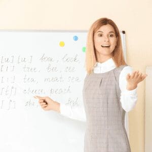 A teacher is standing in front of a whiteboard.