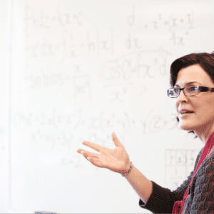 A woman in glasses standing in front of a whiteboard, teaching students at school.