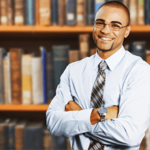 A smiling black teacher standing in front of a bookshelf.