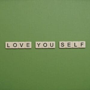 Scrabble tiles on a green background spell out "LOVE YOU SELF.